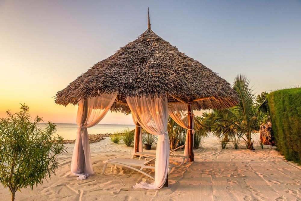 Pavillon de plage au toit de chaume et rideaux blancs, à Zanzibar, au coucher du soleil