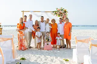 Mariés et famille réunis en tenues orange sur une plage de sable blanc