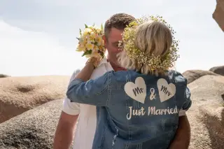Jeunes mariés enlacés, la mariée en veste de jean « Just Married », au milieu des rochers