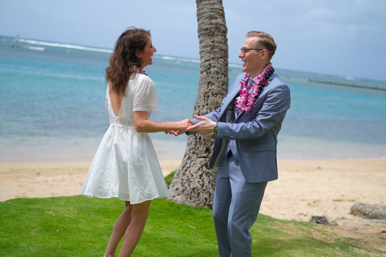 Lucie et Stéphane, mariés à Hawaï, un collier de fleurs au cou, face à face sur la plage