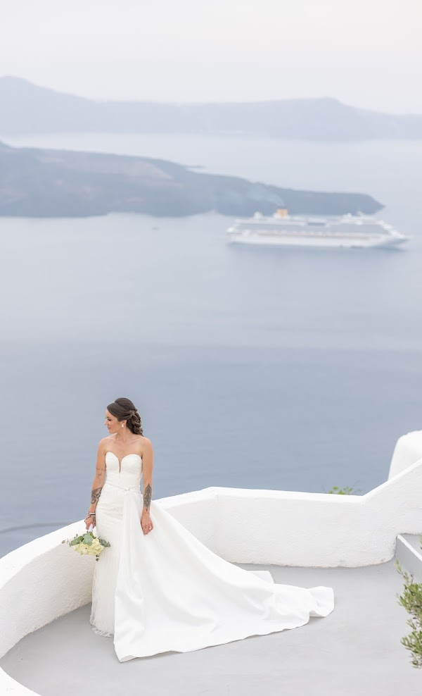 Sandra et Vivien, mariés à Santorin : la mariée devant la caldeira et un bateau de croisière