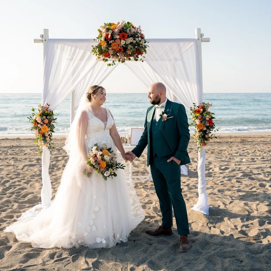 Mariés main dans la main devant une arche de fleurs sur une plage