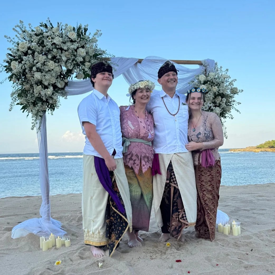 Famille en tenues traditionnelles devant l'arche de la cérémonie balinaise, sur la plage
